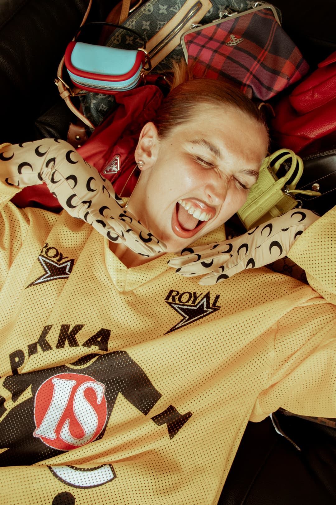 caucasian female with mouth open wide laying on a cluster of hand bags