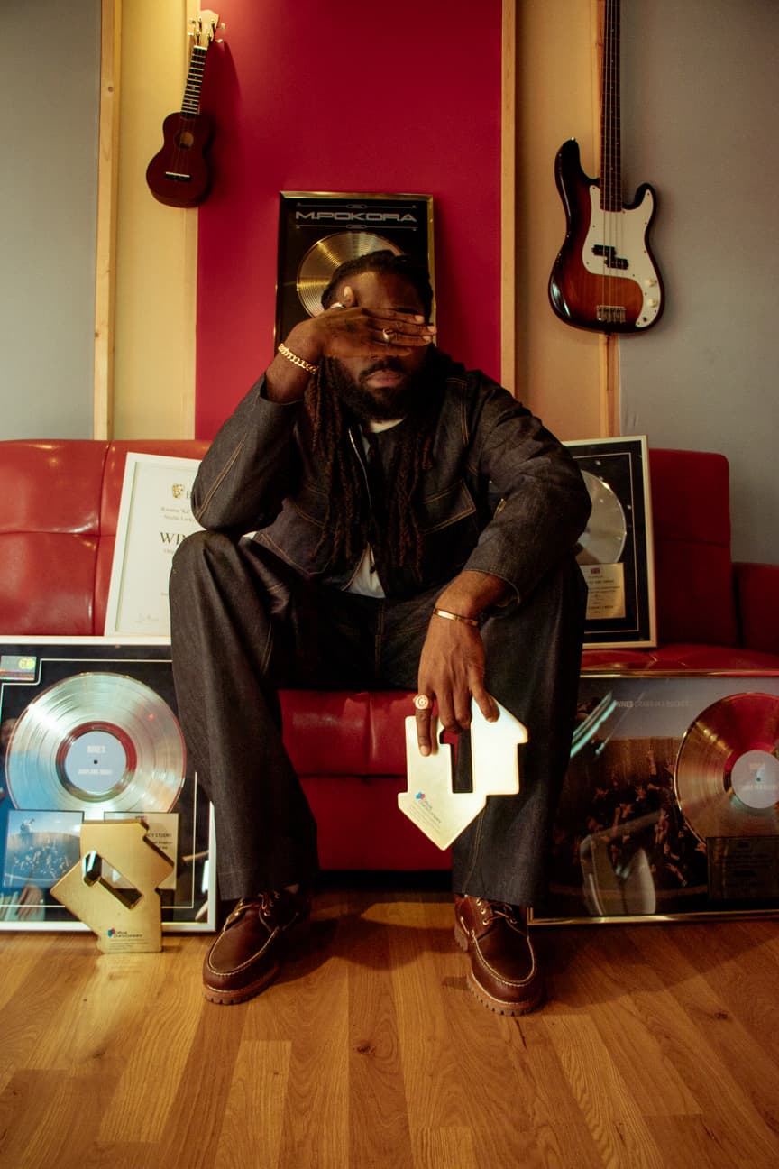 Black man wearing denim, holding a gold ornament, surrounded by other accolades