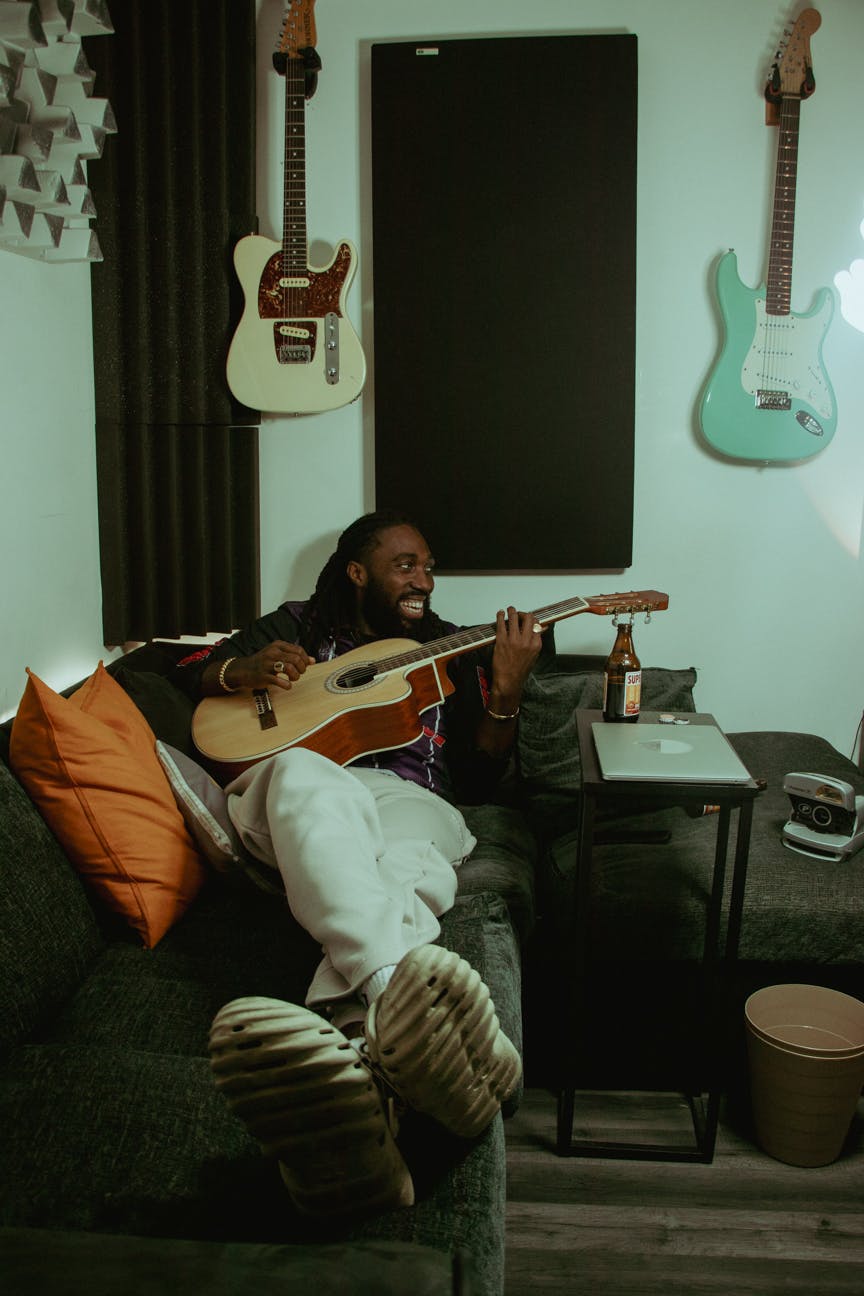 Black man laying in a chair playing a guitar